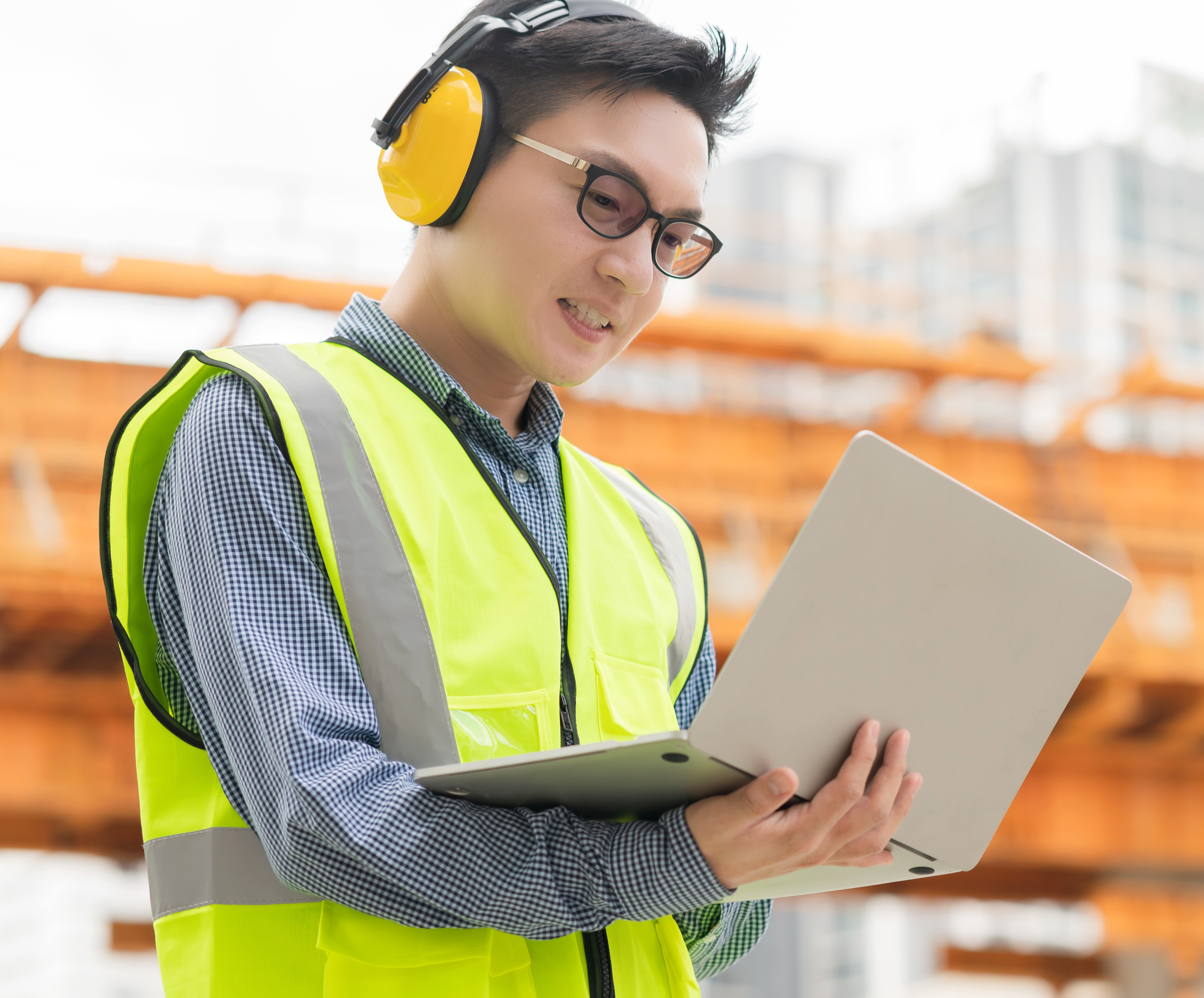 smart-asian-male-professional-civil-engineer-hand-hold-laptop-site-construction-check-with-infastrcture-building-background